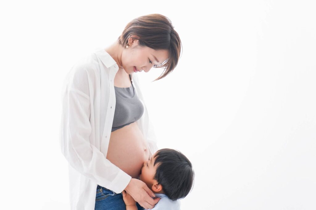 妊婦のお腹にキスをする息子。温かい母子の愛情が伝わる光景。
