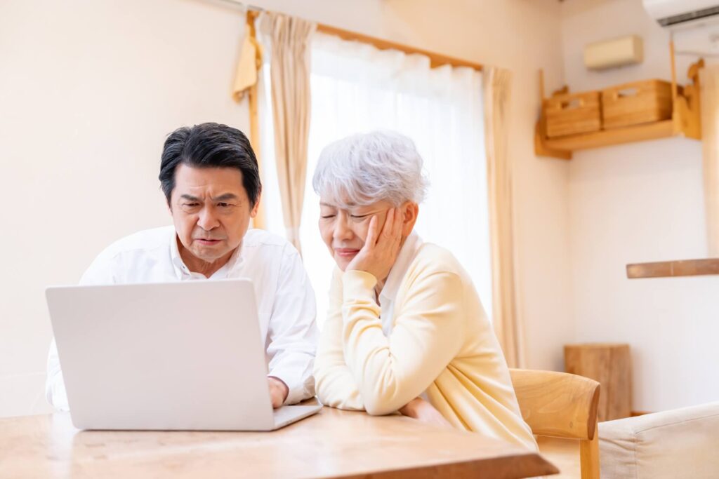 パソコン画面を前に、困ったような表情で悩む高齢夫婦
